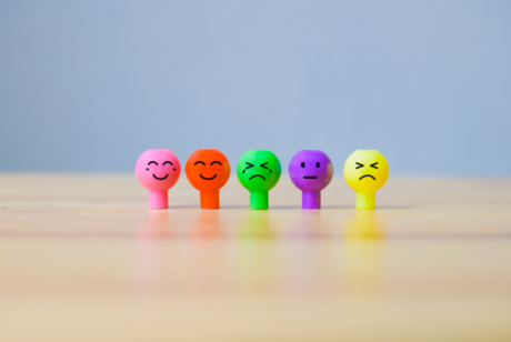 A line of differently colored pencil toppers shaped like faces depict different emotions.